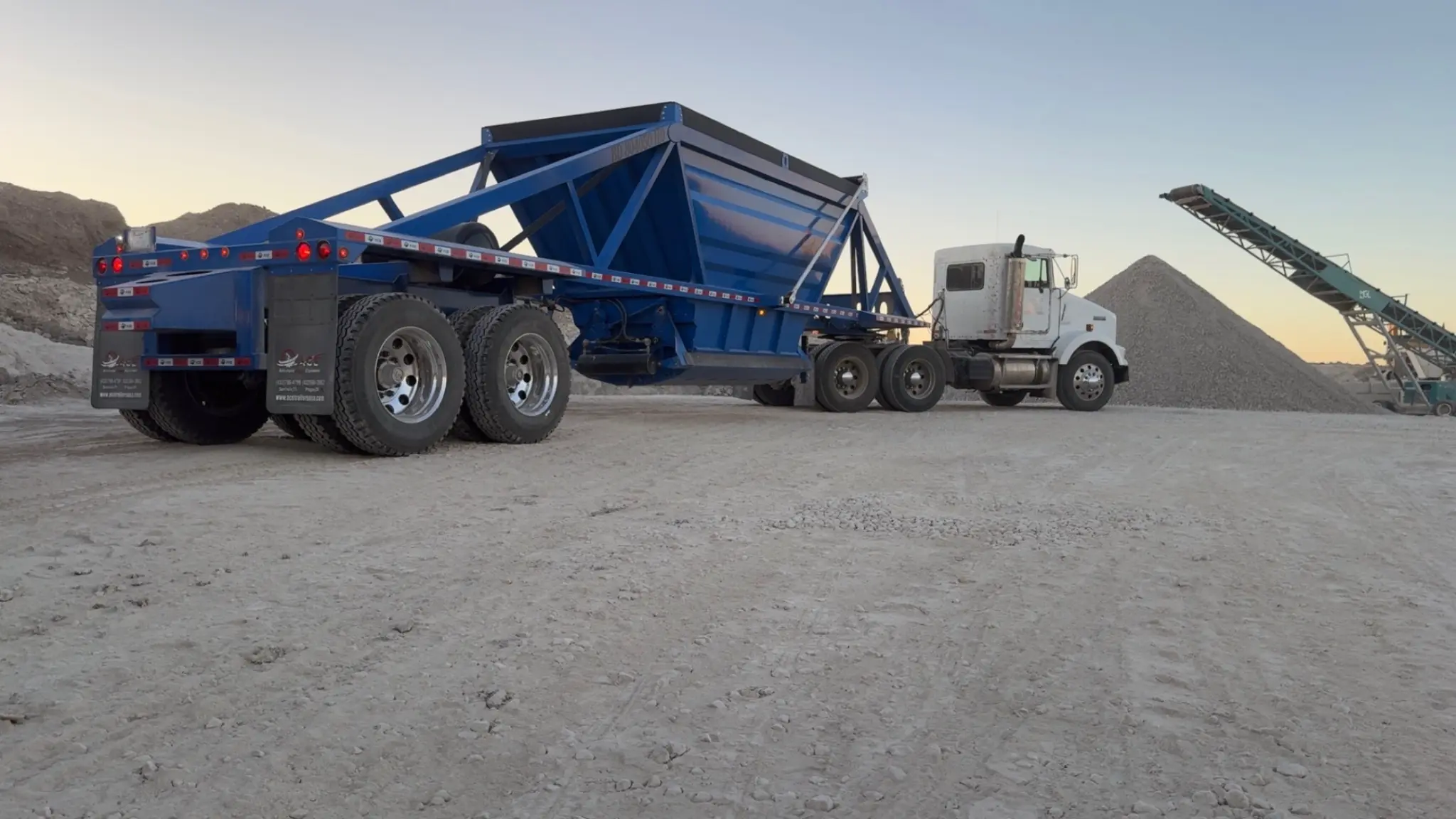 Plus One belly dump truck delivering and spreading limestone road base on ranch road
